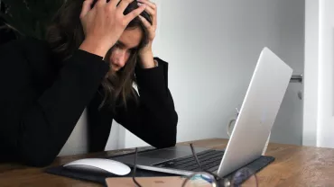 Personne assise à un bureau avec un ordinateur portable, semblant stressée.