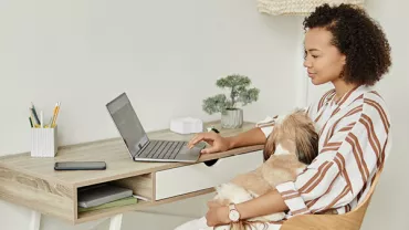 Personne à un bureau avec un ordinateur portable et un chien sur les genoux
