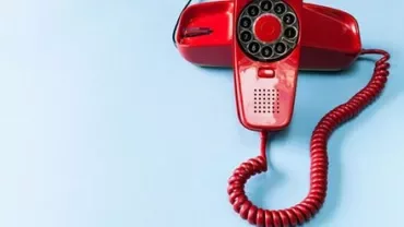 Red rotary phone on light blue background.