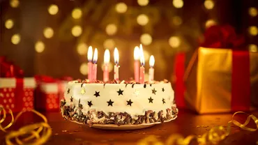 A birthday cake with lit candles and gift boxes in the background.