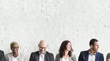 People seated against a white brick wall, smiling.