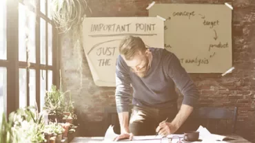 Personne écrivant à un bureau avec des papiers et des plantes, brainstorming sur un tableau.
