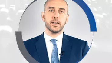 Une personne en costume avec un micro, parlant.