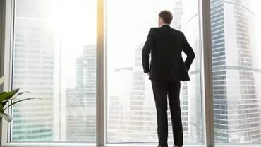Person in a suit looking out at city skyscrapers through a large window.