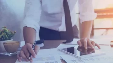 Person working at a desk with documents, tablet, and coffee.