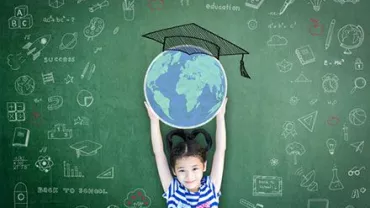 Child holding globe with a graduation cap drawn on chalkboard behind.
