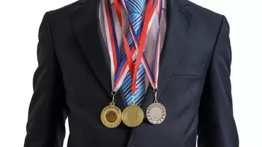 Person in a suit wearing three medals around their neck.