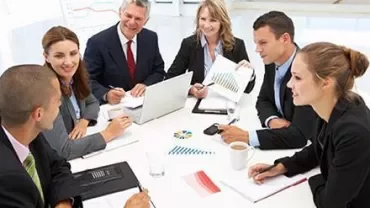 Groupe de professionnels en réunion autour d'une table avec ordinateurs portables et graphiques.