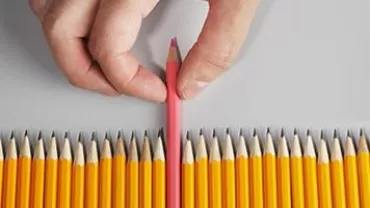 A hand picking a red pencil among yellow pencils.
