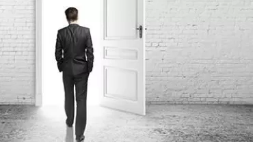 A person in a suit walking through an open door towards a bright light.