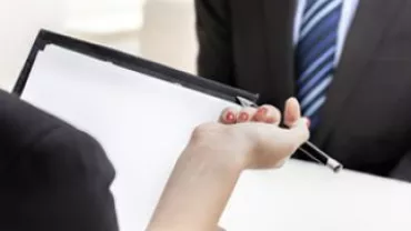 Person holding clipboard and pen during a meeting.