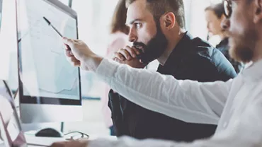 Two people focused on a computer screen with graphs.