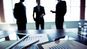 Business meeting with charts on table, silhouettes in background.