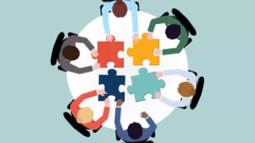 Group of people seated around a table, assembling colorful puzzle pieces.