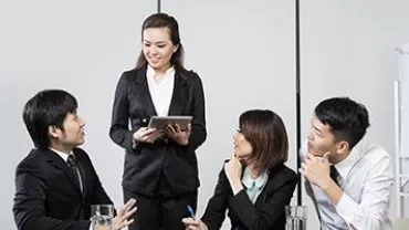 Group of people in a business meeting, one standing with a tablet.