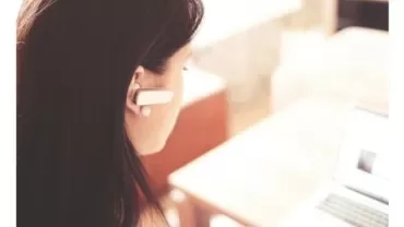 Personne utilisant un ordinateur portable avec une oreillette sans fil.