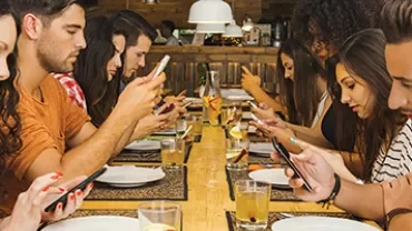 A group of people sitting at a long table using smartphones.