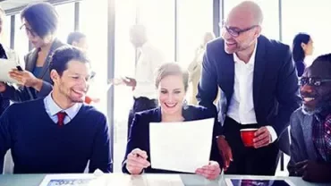 Groupe de personnes en réunion, souriant et examinant des documents.