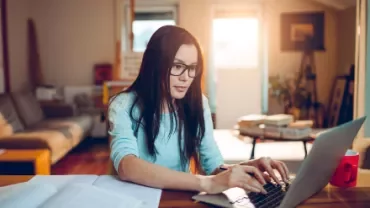 Person working on a laptop at a home office with books.