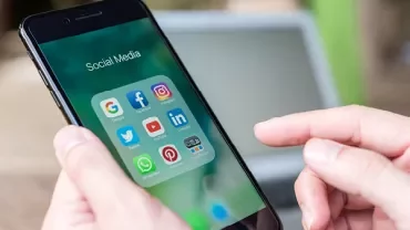 Personne tenant un smartphone avec des icônes de réseaux sociaux.