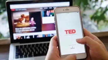 Personne utilisant un téléphone avec l'application TED ouverte, ordinateur portable en arrière-plan.
