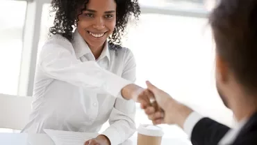 Personne souriante serrant la main de quelqu'un à travers une table avec une tasse de café.