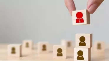 Wooden blocks with person icons stacked, one lifted by a hand.