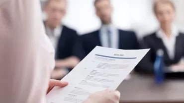 Une personne tient un CV devant des intervieweurs à une table.