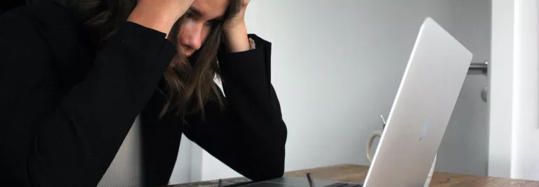 Personne assise à un bureau avec un ordinateur portable, semblant stressée.