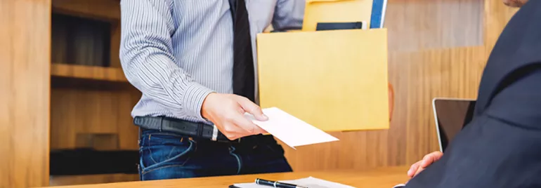 Personne tendant une enveloppe à quelqu'un assis à un bureau.