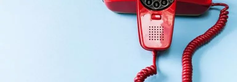 Red rotary phone on light blue background.