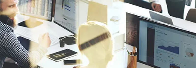 Personnes travaillant à des bureaux avec des ordinateurs affichant des graphiques.