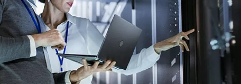 Two people in a server room reviewing information on a laptop.
