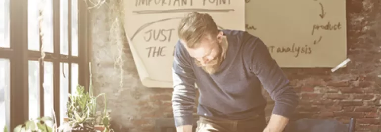 Person writing at a desk with papers and plants, brainstorming ideas on a board.