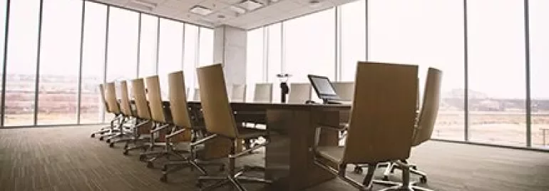 Salle de conférence vide avec table et chaises, grandes fenêtres.