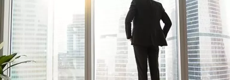 Personne en costume regardant des gratte-ciels à travers une grande fenêtre.