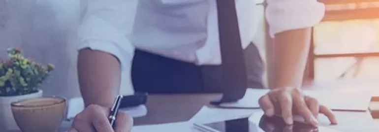 Personne travaillant à un bureau avec des documents, une tablette et un café.
