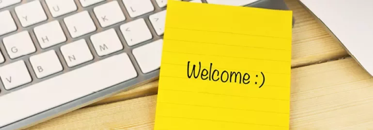 Sticky note with 'Welcome :)' next to a keyboard and pen.
