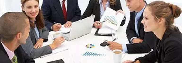 Group of professionals having a meeting around a table with laptops and charts.