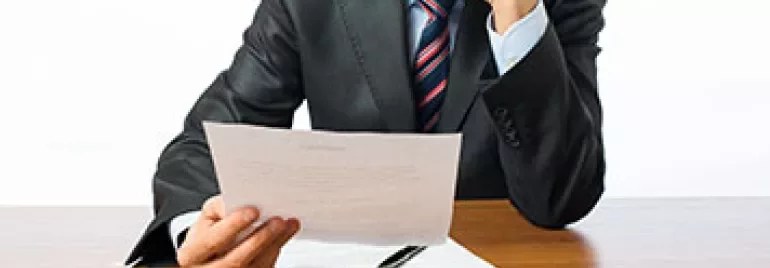 Personne en costume lisant un document à une table en bois.