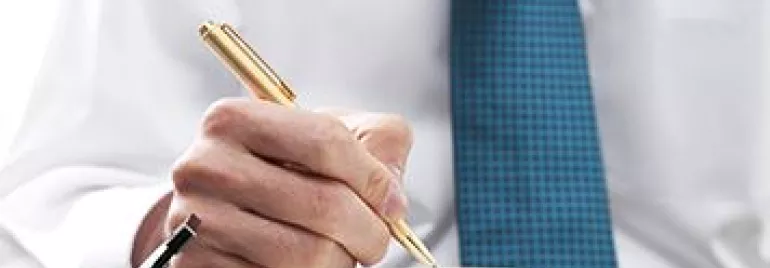 Person writing in a planner with a pen, wearing a blue tie.