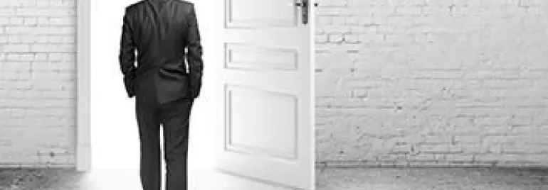 A person in a suit walking through an open door towards a bright light.
