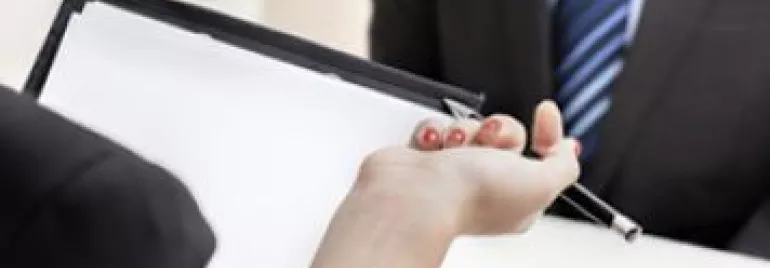 Person holding clipboard and pen during a meeting.