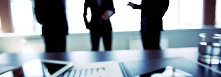 Business meeting with charts on table, silhouettes in background.