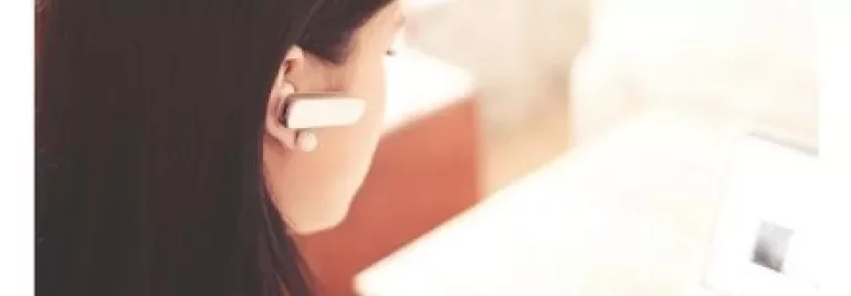 Person using a laptop while wearing a wireless earpiece.