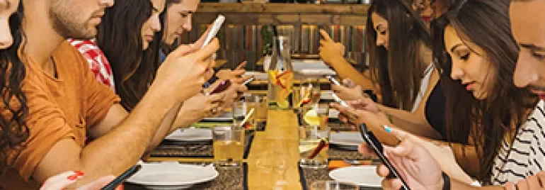A group of people sitting at a long table using smartphones.