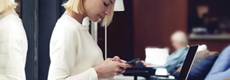 Personne en pull blanc utilisant un smartphone, assise près d'un ordinateur portable.