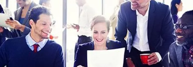 Groupe de personnes en réunion, souriant et examinant des documents.