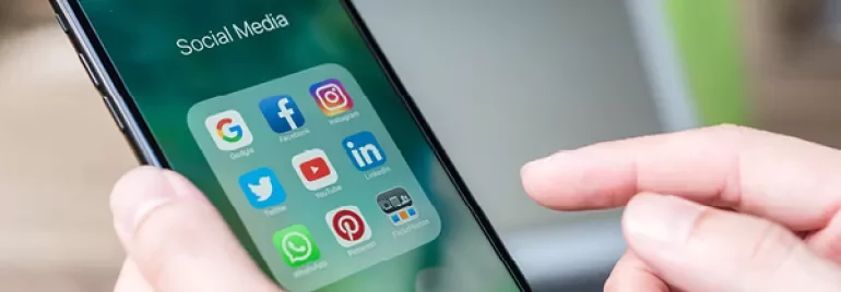 Personne tenant un smartphone avec des icônes de réseaux sociaux.