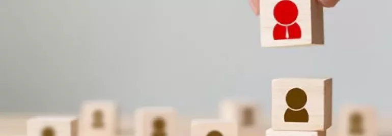 Wooden blocks with person icons stacked, one lifted by a hand.